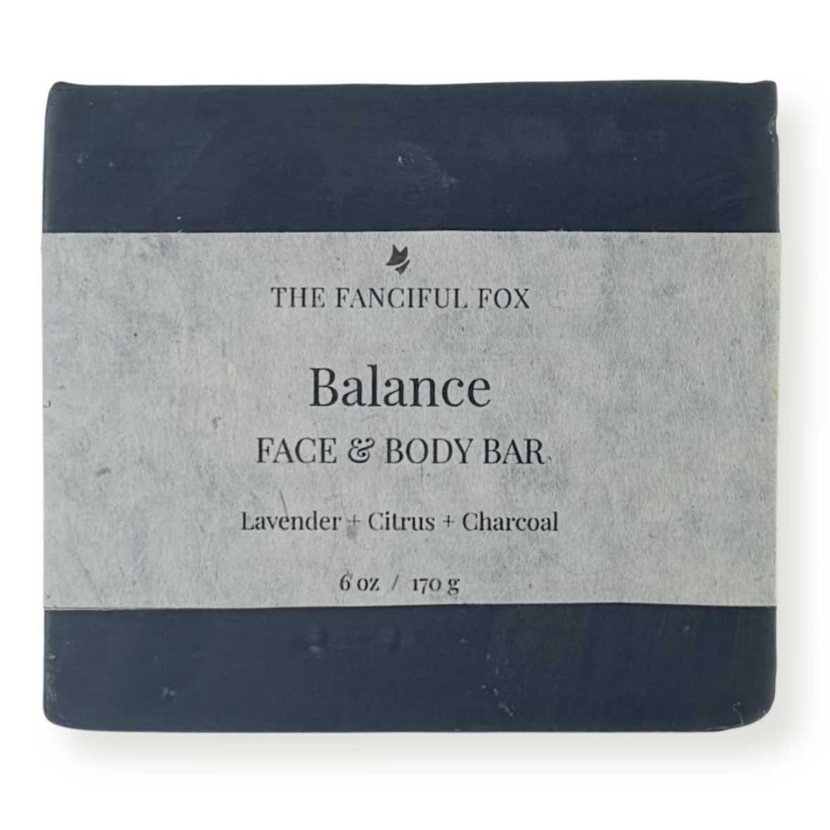 A rectangular bar of soap wrapped in a light gray paper label, with dark navy blue top and bottom bands. The label reads 'THE FANCIFUL FOX Balance FACE & BODY BAR' and 'Lavender + Citrus + Charcoal'.