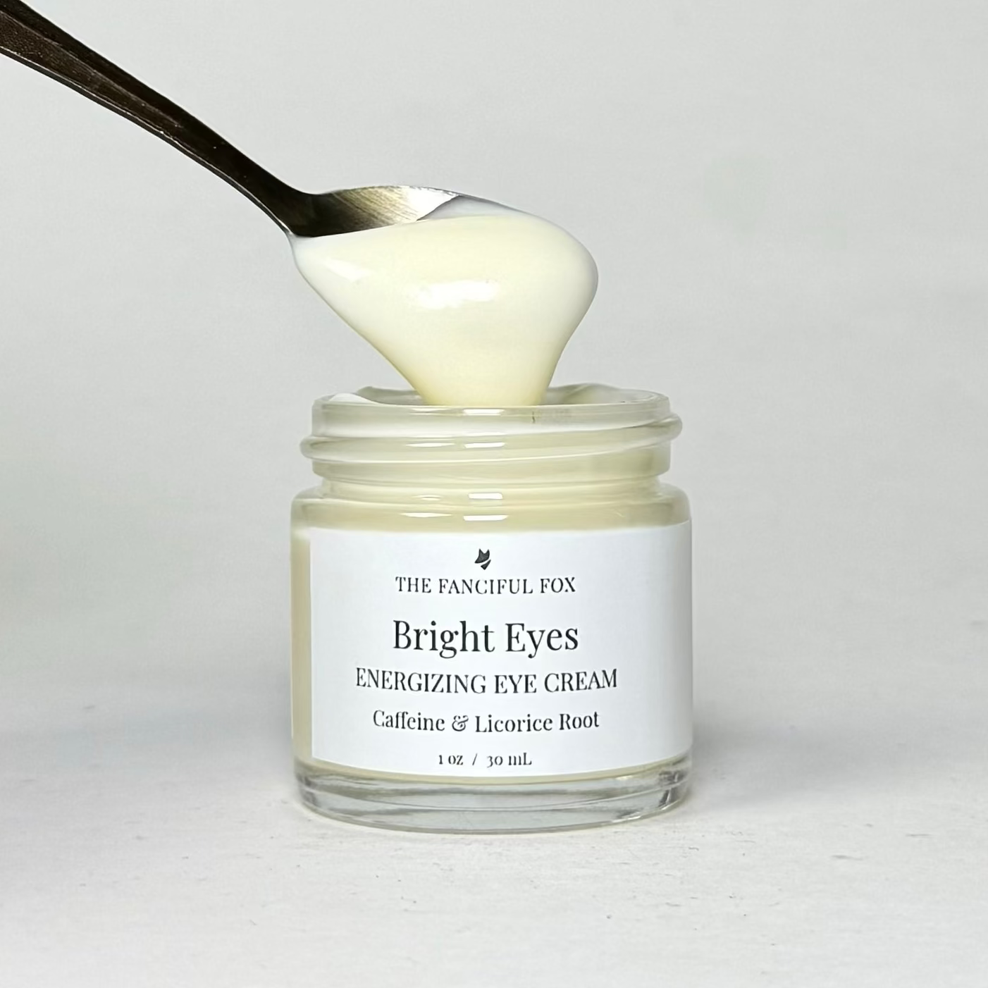 Jar of 'Bright Eyes' eye cream with a spoon scooping out some cream, on a light gray background.