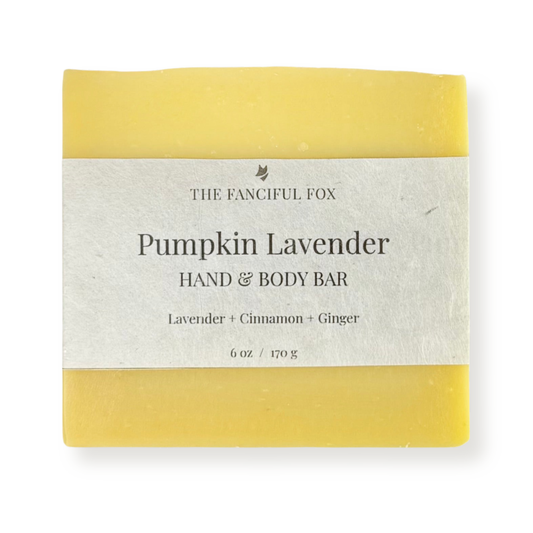 A rectangular hand and body bar of soap wrapped in a light gray paper label. The soap has yellow ends and is labeled 'Pumpkin Lavender HAND & BODY BAR' by 'THE FANCIFUL FOX'.