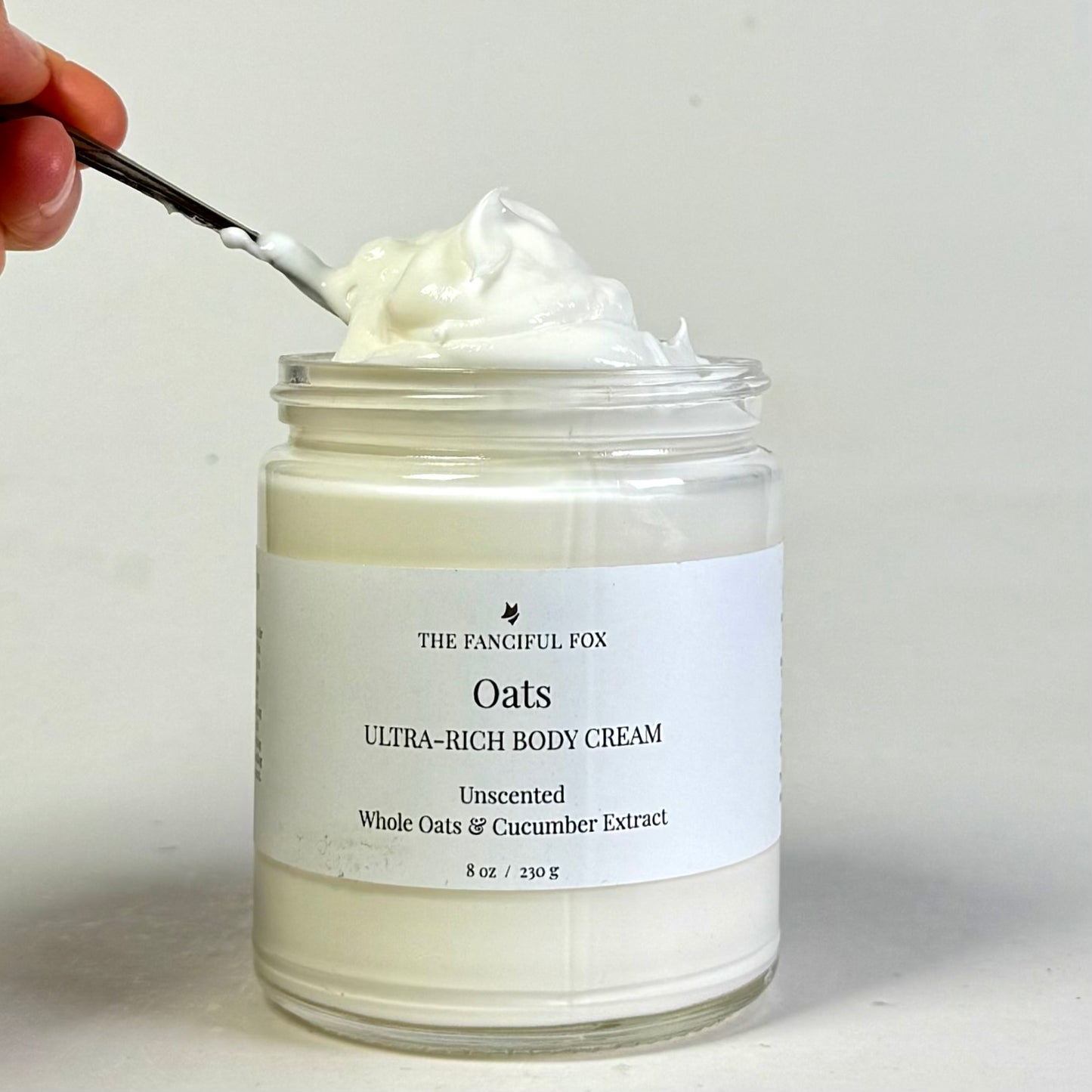 Jar of Oats Ultra-Rich Body Cream with a spoonful being taken, on a neutral background.